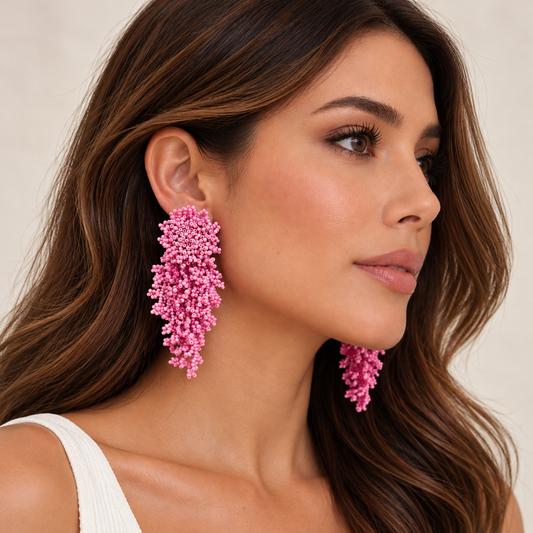 A close-up of a woman wearing large, chunky pink beaded drop earrings with a textured, coral-like design. The earrings are made of small, bright pink beads.